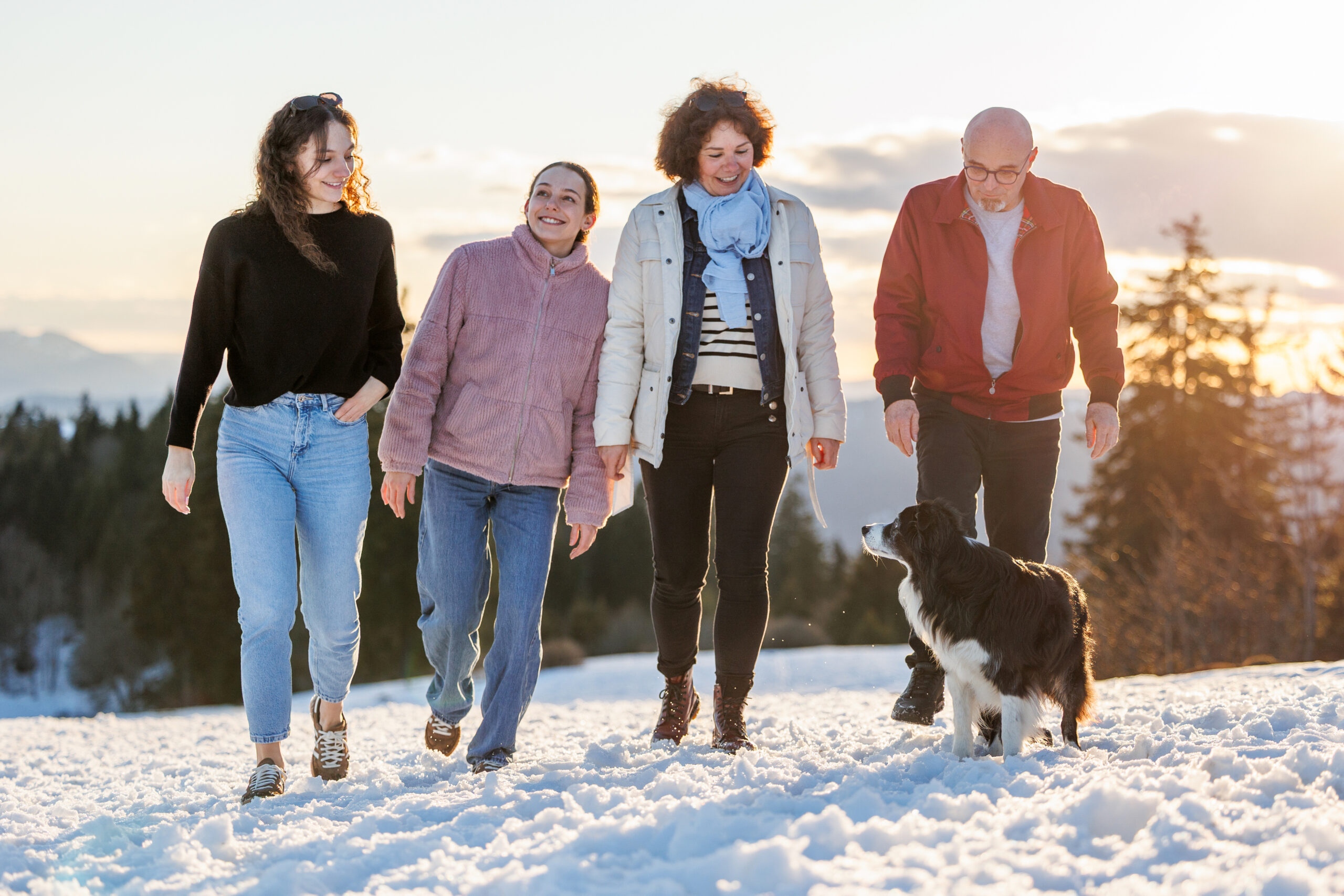 Famille de 4 humains et un chien qui marchent dans la neige au soleil couchant lors de leur séance photo dans le canton de Neuchâtel en Suisse.