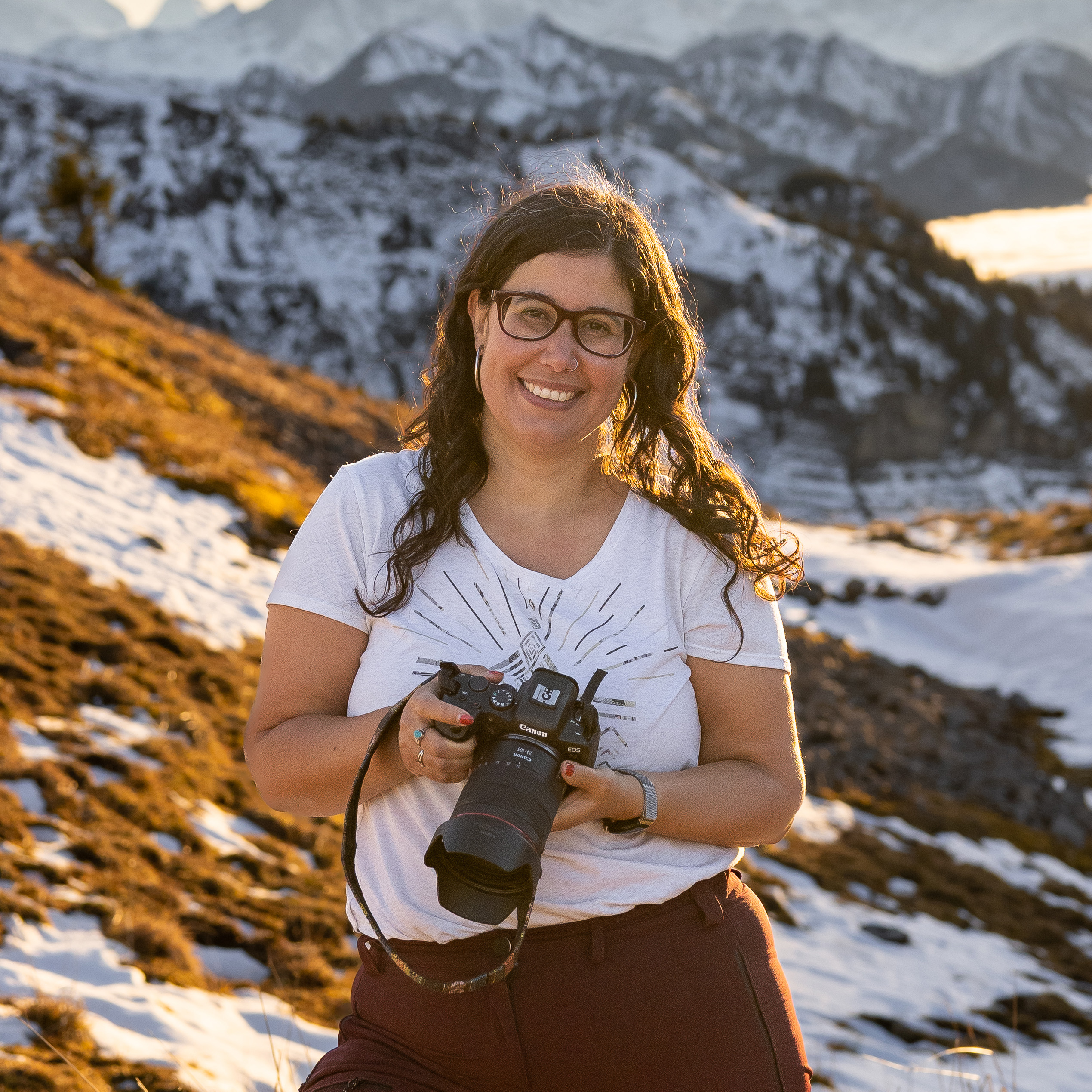 Sofia photographe pour les chiens et leurs humains en Suisse qui pose avec son appareil photo devant les montagnes suisses au soleil couchant.